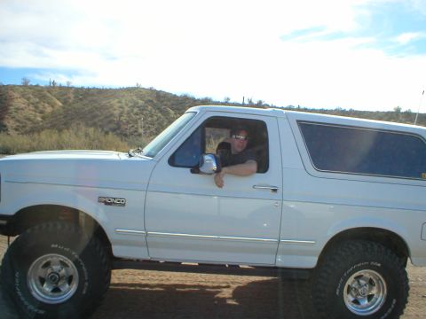 1993 Ford Bronco - A person leans out the window of a white Ford Bronco parked in a dry, hilly area.