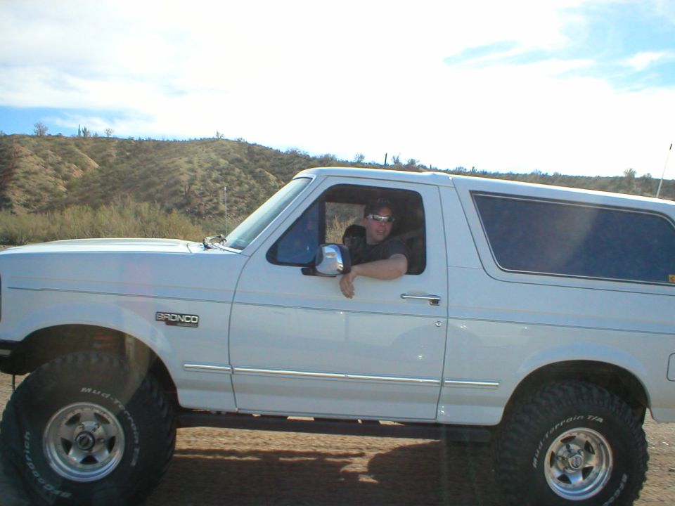 White lifted 1990s Ford Bronco in side view with driver, in desert setting