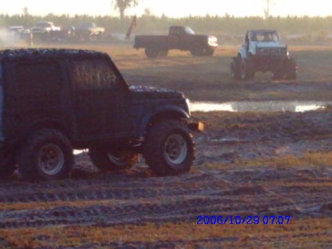 1987 Suzuki Samurai - Multiple off-road vehicles are seen in a muddy field during the day.