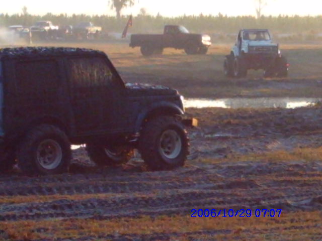 Black 1987 Suzuki Samurai in mud, 3/4 front view, with other vehicles in background