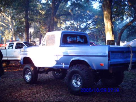 1987 Suzuki Samurai - Two pickup trucks are parked outdoors among trees. One is a lifted blue and white truck.
