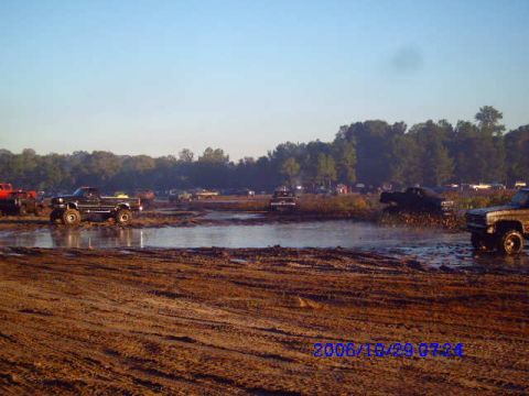 1987 Suzuki Samurai - Multiple trucks are seen navigating a muddy terrain under a clear sky.