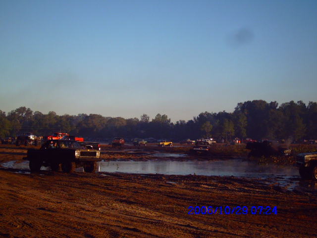 Muddy trucks in a mud pit with trees and a clear blue sky
