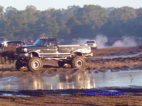 1987 Suzuki Samurai - A lifted pickup truck navigates a muddy track, with other vehicles visible in the distance.