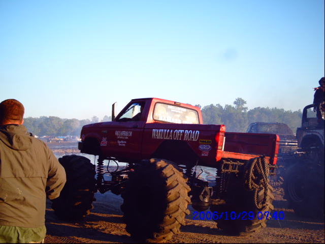Red monster truck with 'Wakulla Off Road' text on door, large tires, and another vehicle behind it