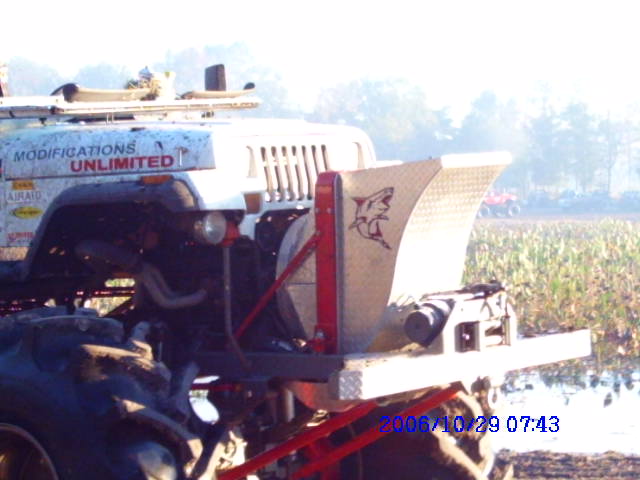White Jeep with "MODIFICATIONS UNLIMITED" text, large rear spreader attachment, and oversized tires