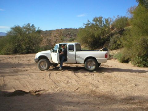 1993 Ford Bronco - A white pickup truck is parked on a dirt road, with a person sitting in the open driver's door.