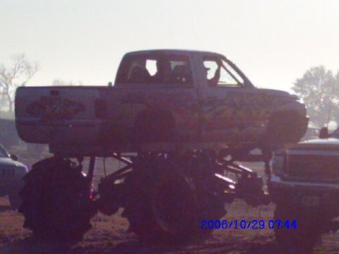 1987 Suzuki Samurai - A lifted pickup truck with oversized tires sits in a muddy area, with another vehicle nearby.
