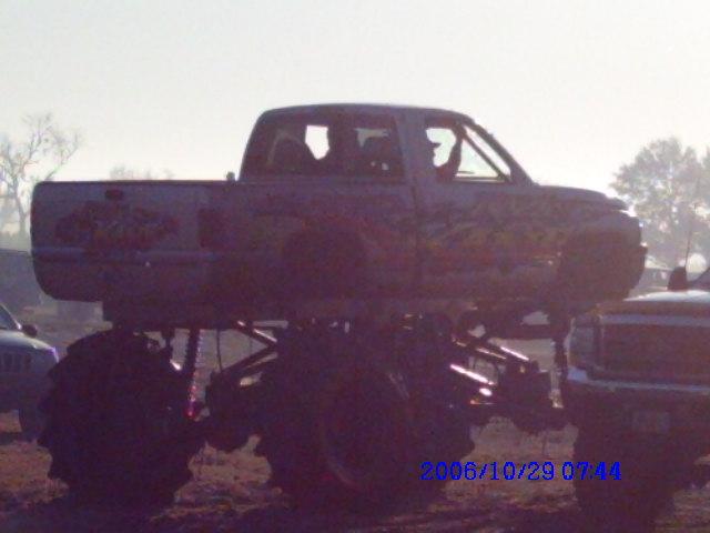 Monster truck with large tires, side view. Another truck is partially visible on the right