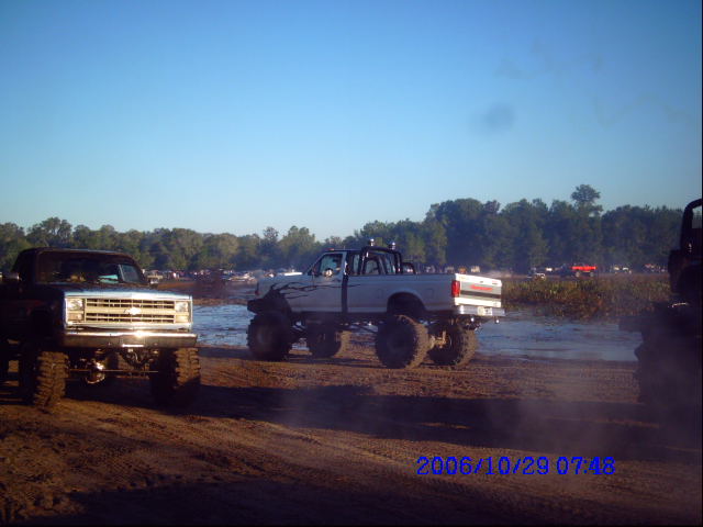 Two lifted pickup trucks are parked in a muddy area with trees in the background. A timestamp reads 2006/10/29 07:48