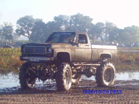 1987 Suzuki Samurai - This lifted pickup truck is covered in mud and appears to be stuck in a muddy field.