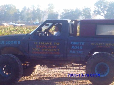 1987 Suzuki Samurai - Modified pickup truck with custom text and large off-road tires is parked in a field.