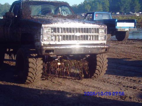 1987 Suzuki Samurai - A heavily mud-covered pickup truck is shown from the front, with another truck in the background.