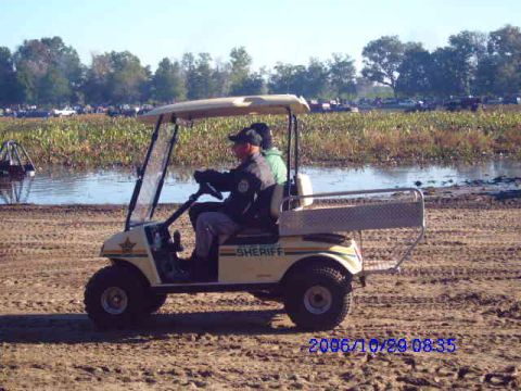 1987 Suzuki Samurai - A golf cart with "SHERIFF" markings is driven across a dirt path near a body of water.
