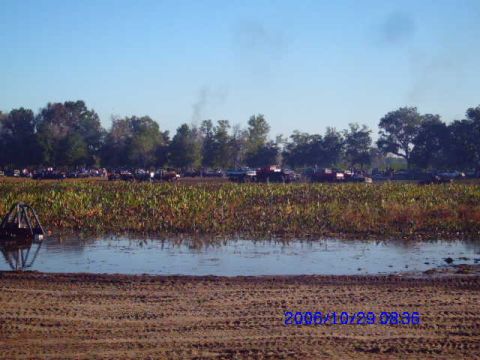 1987 Suzuki Samurai - A collection of vehicles are gathered in a muddy, vegetated area under a clear blue sky.