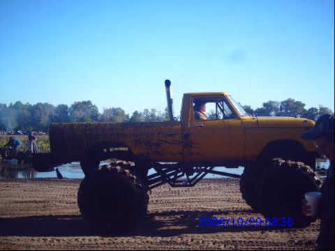 1987 Suzuki Samurai - A yellow monster truck is parked on a dirt track under a clear blue sky.
