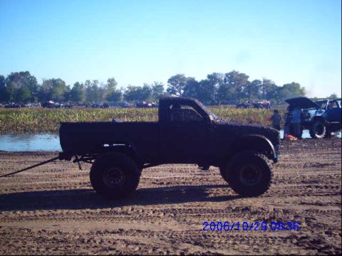 1987 Suzuki Samurai - A black pickup truck is seen being towed from a muddy area with other vehicles in the background.
