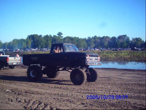 1987 Suzuki Samurai - Lifted pickup truck with large tires on a dirt track near water. Another truck is visible to the left.