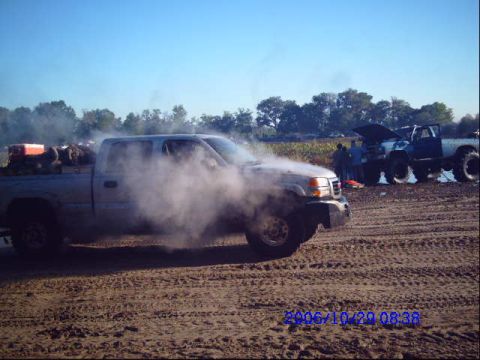 1987 Suzuki Samurai - A pickup truck is seen emitting a large amount of smoke while another lifted truck is parked nearby.