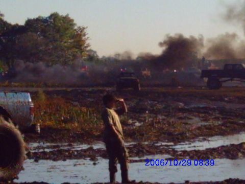 1987 Suzuki Samurai - A muddy field is filled with trucks and smoke, with a person observing the scene.