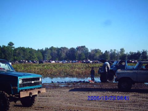 1987 Suzuki Samurai - Multiple off-road vehicles gathered in a muddy field under a clear blue sky.