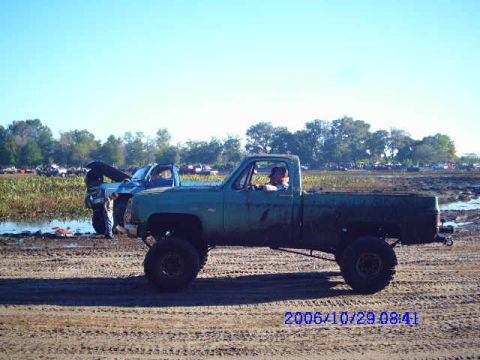 1987 Suzuki Samurai - A green pickup truck is parked on a dirt track with another blue truck in the background.