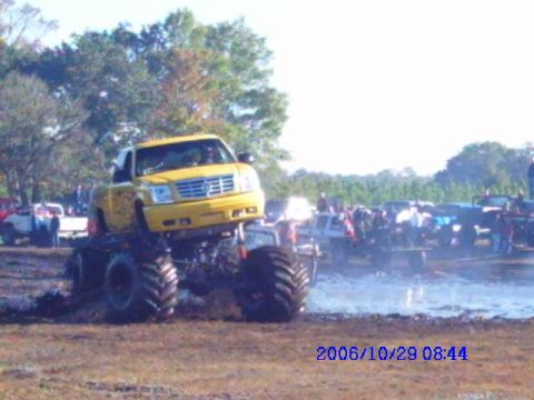 1987 Suzuki Samurai - Monster truck event with multiple vehicles and spectators in a muddy field.