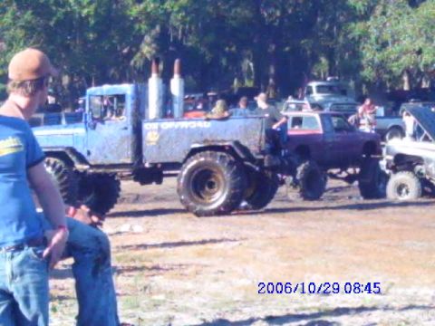 1987 Suzuki Samurai - Multiple lifted trucks and SUVs at a mud bogging event with spectators.