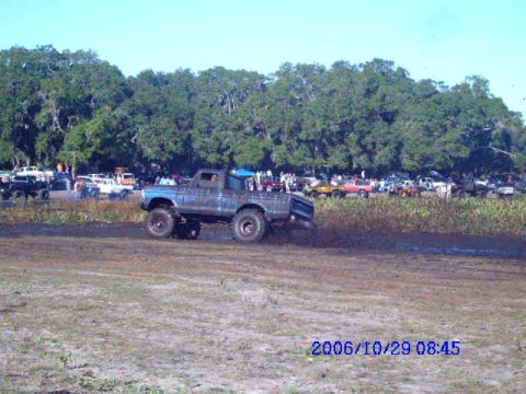 1987 Suzuki Samurai - A lifted blue truck navigates a muddy track with spectators and other vehicles nearby.