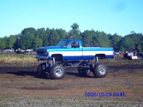 1987 Suzuki Samurai - A lifted pickup truck with a two-tone paint job is shown in a muddy outdoor area.