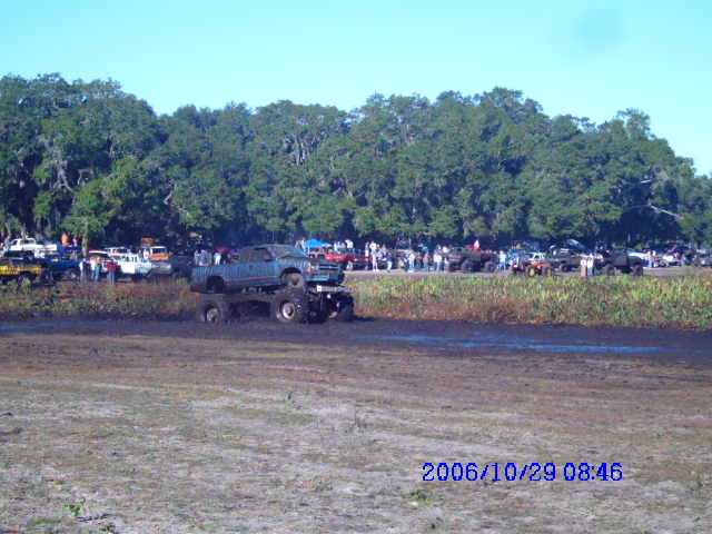 Mud bog event with several monster trucks and spectators in the background