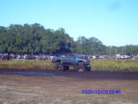 1987 Suzuki Samurai - A modified pickup truck navigates a muddy track with spectators and other vehicles in the distance.