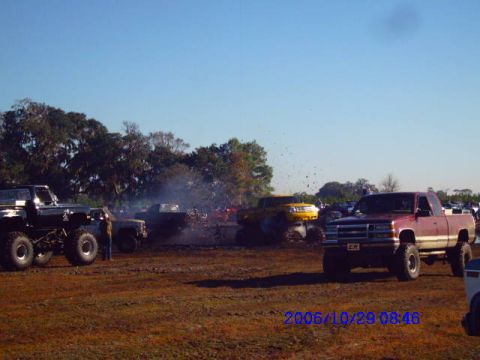 1987 Suzuki Samurai - Multiple trucks are engaged in a mud bogging event under a clear blue sky.