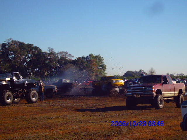 Red pickup truck with white stripe, lifted, in mud pit