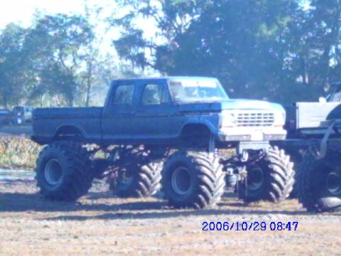 1987 Suzuki Samurai - A blue monster truck with oversized tires is parked outdoors, with another vehicle partially visible to its right.