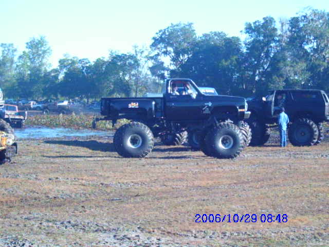 Black monster truck with large tires parked on muddy ground