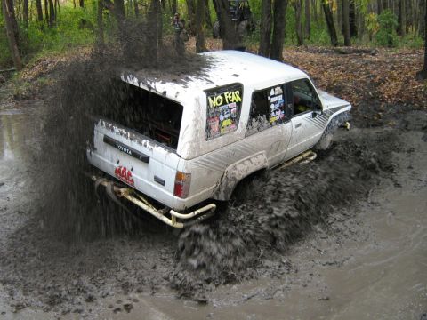 1990 Ford Bronco - This Toyota 4Runner is navigating a challenging muddy terrain, kicking up a large spray.