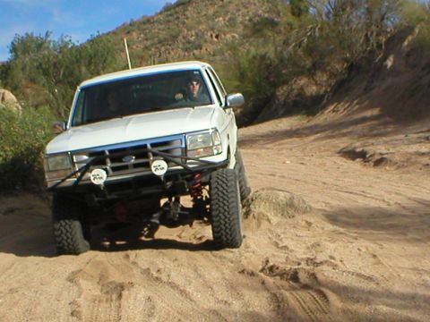 1993 Ford Bronco - A white Ford Bronco navigates a rocky, dirt path in a dry, hilly landscape.