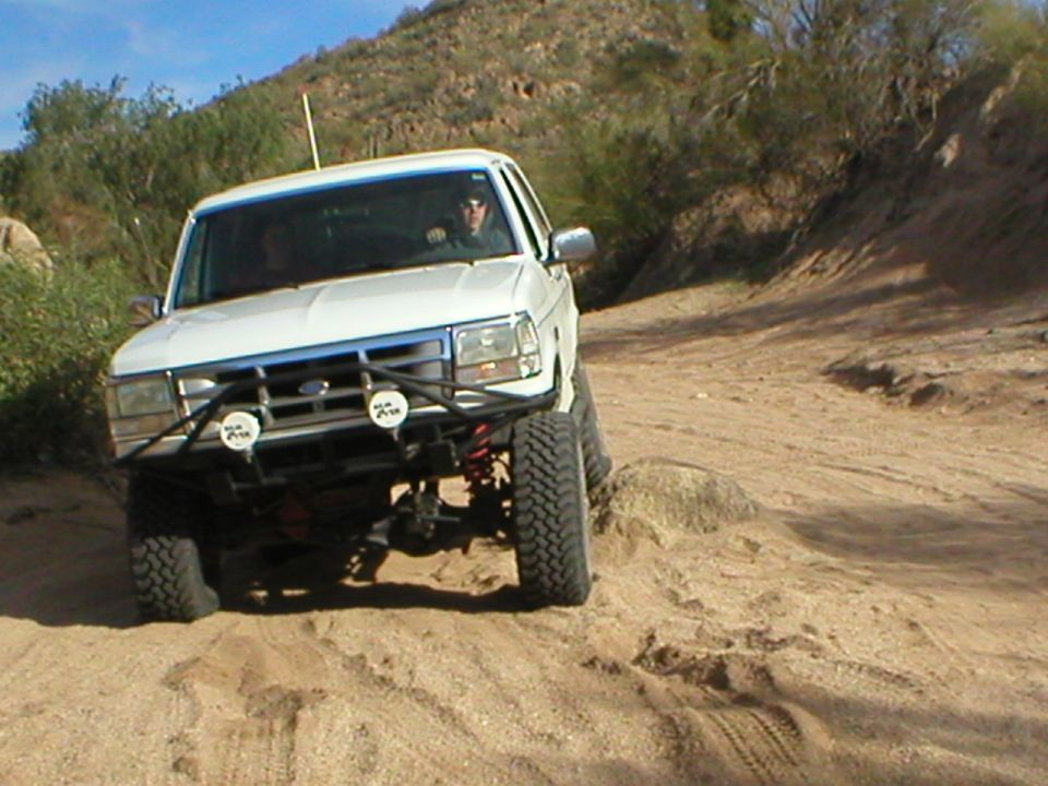 White lifted Bronco with tube brush guard and driving lights climbing a sandy desert wash