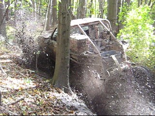 1990 Ford Bronco - An off-road vehicle is deeply stuck in the mud and trees, its body covered in dirt.
