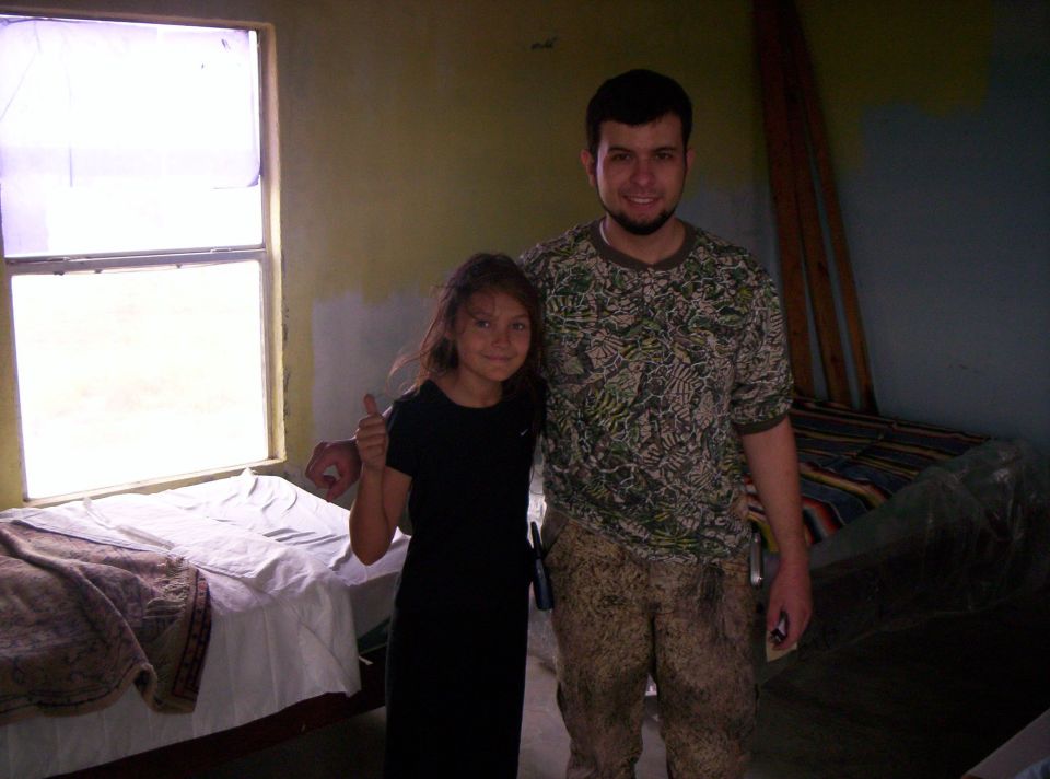 A girl giving a thumbs-up beside a man in a camo shirt in a room with mattresses