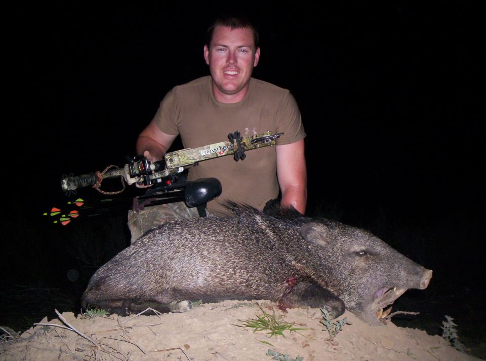Hunter with camo Bowtech bow posing at night behind a harvested javelina