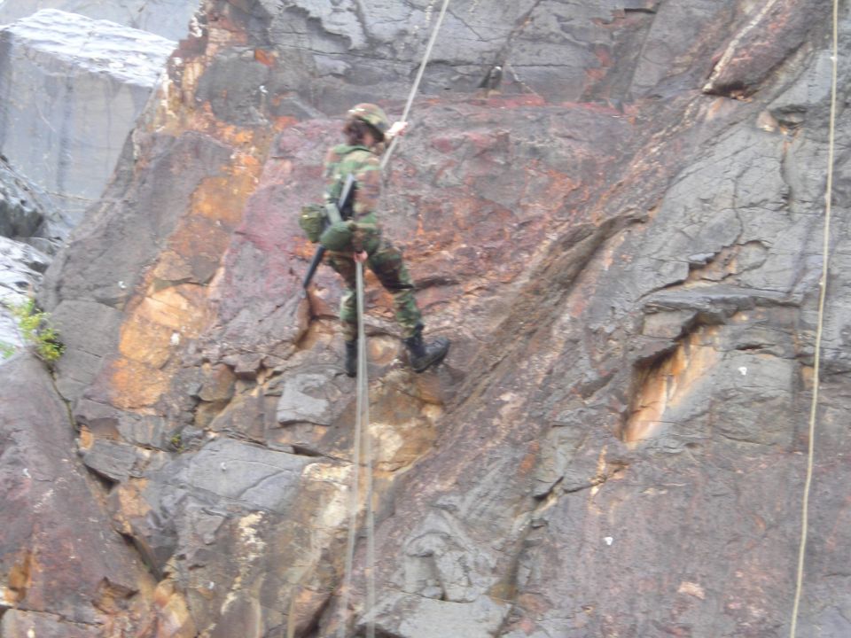 Person in camouflage rappelling down a rock face with ropes