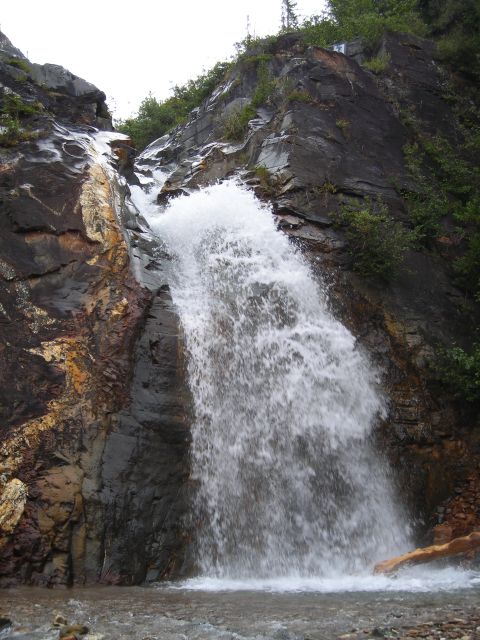 2003 Jeep TJ - A powerful waterfall plunges over a cliff face into a pool below, surrounded by natural rock formations and vegetation.