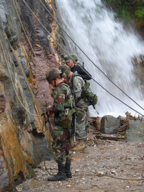 2003 Jeep TJ - Several individuals in military attire prepare to rappel down a wet, rocky cliff beside a cascading waterfall.