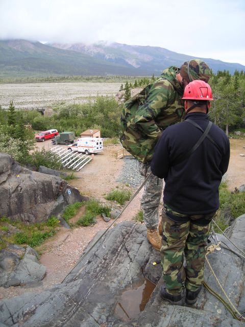 2003 Jeep TJ - A red pickup truck and an ambulance are visible in the distance, parked near a rocky terrain with a mountainous backdrop.