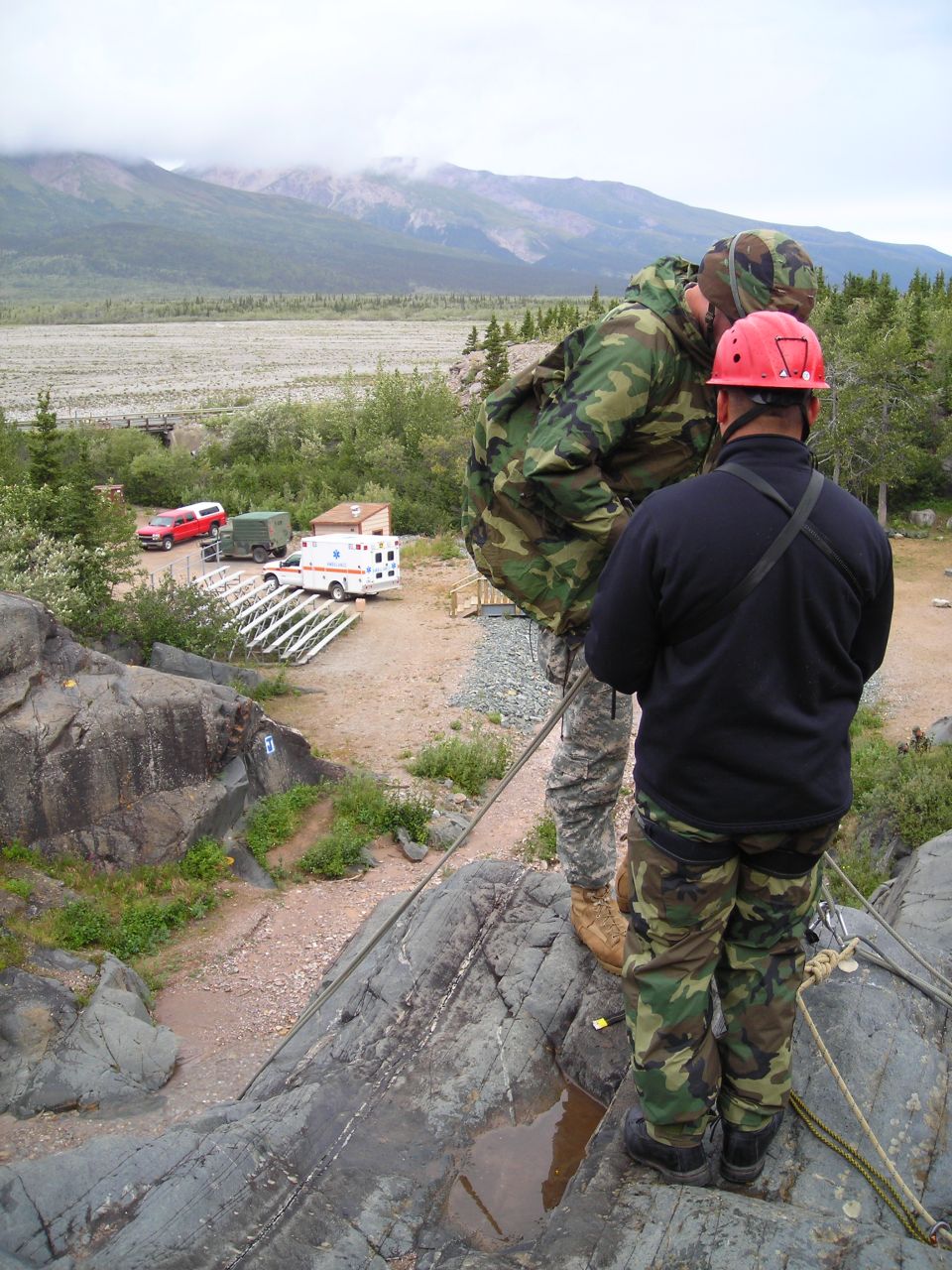 Red pickup truck and ambulance parked near a rocky area with mountains in the background