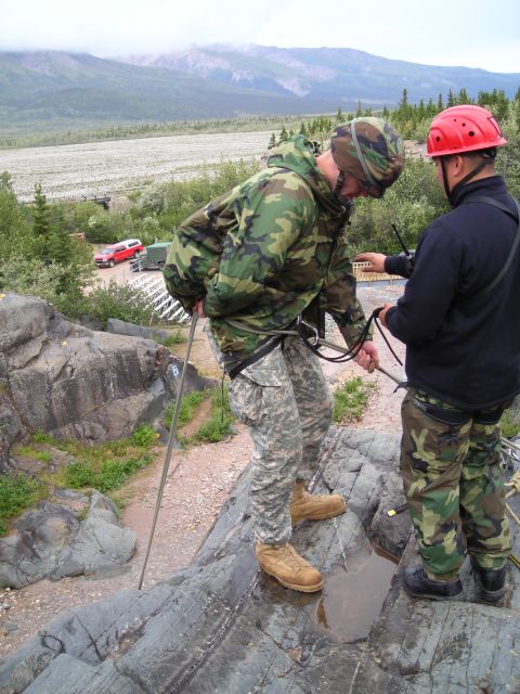 2003 Jeep TJ - Two individuals are engaged in rappelling preparation on a rocky outcrop with a scenic mountain backdrop.