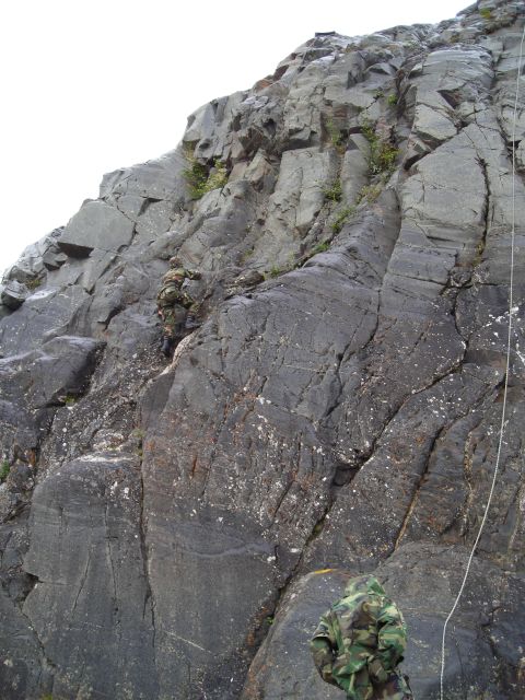 2003 Jeep TJ - Two individuals in camouflage gear are engaged in rock climbing on a steep, cliff face.