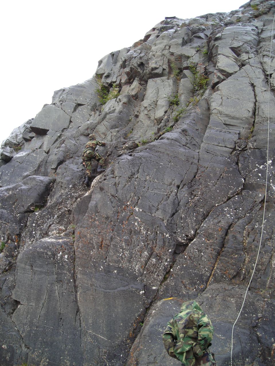 Rock climbing scene with two people in camouflage, one ascending a cliff face